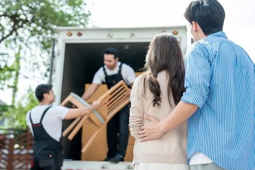 A couple watching their household items being loaded into a moving truck.