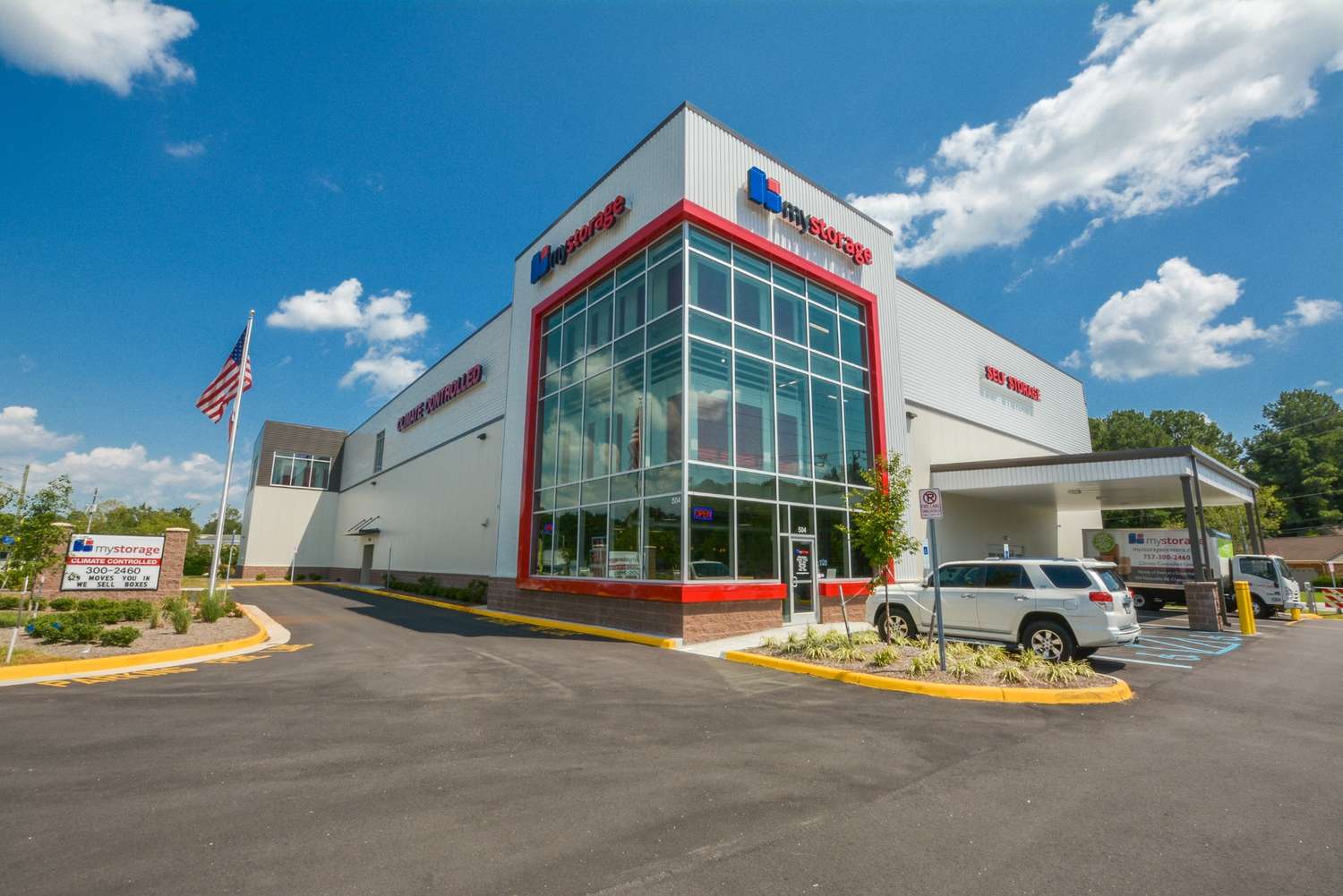 Exterior view of a modern self-storage facility with a large parking area and clear sky in the background.